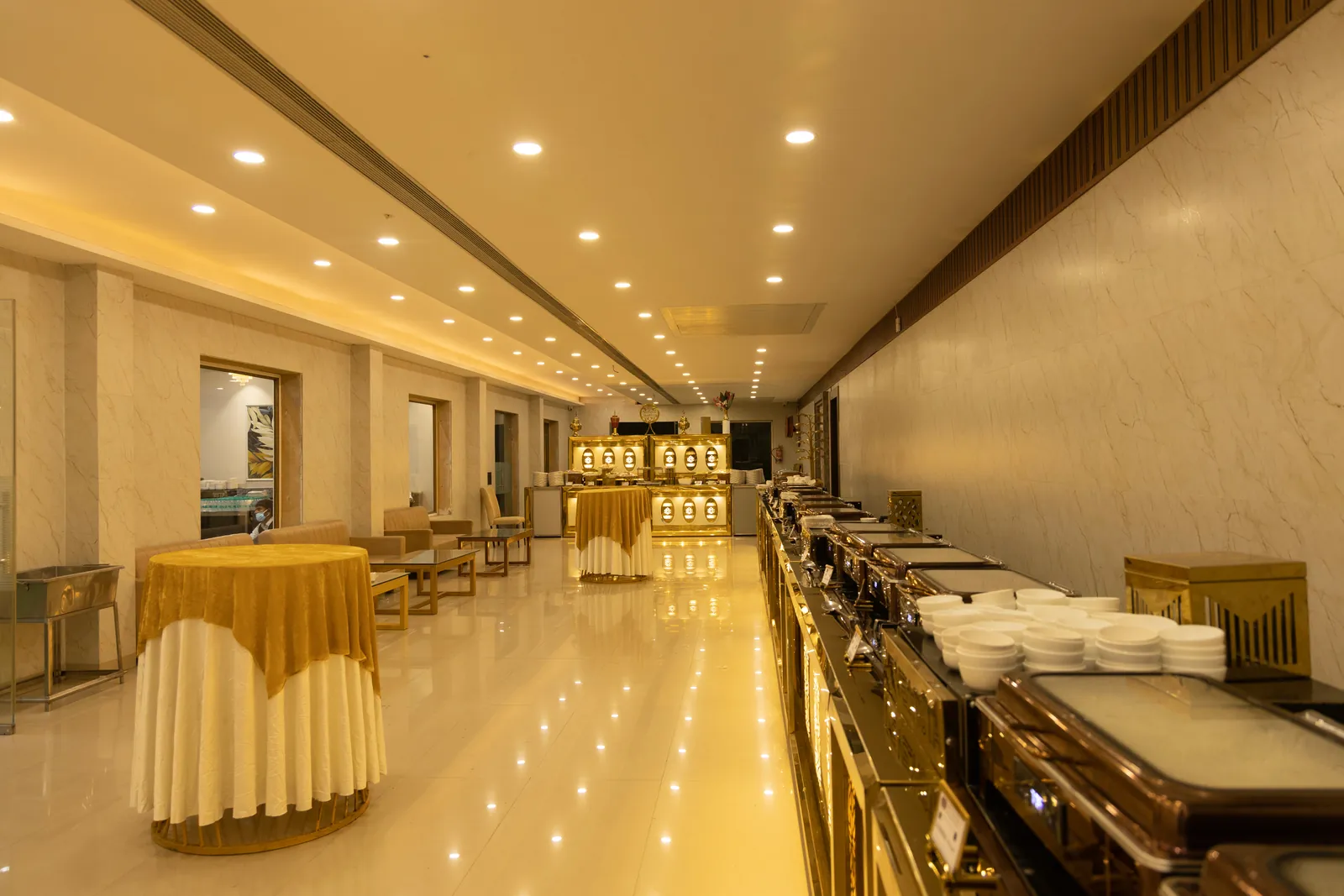 Buffet counter with chafing dishes and stacked plates in a warmly lit hall
