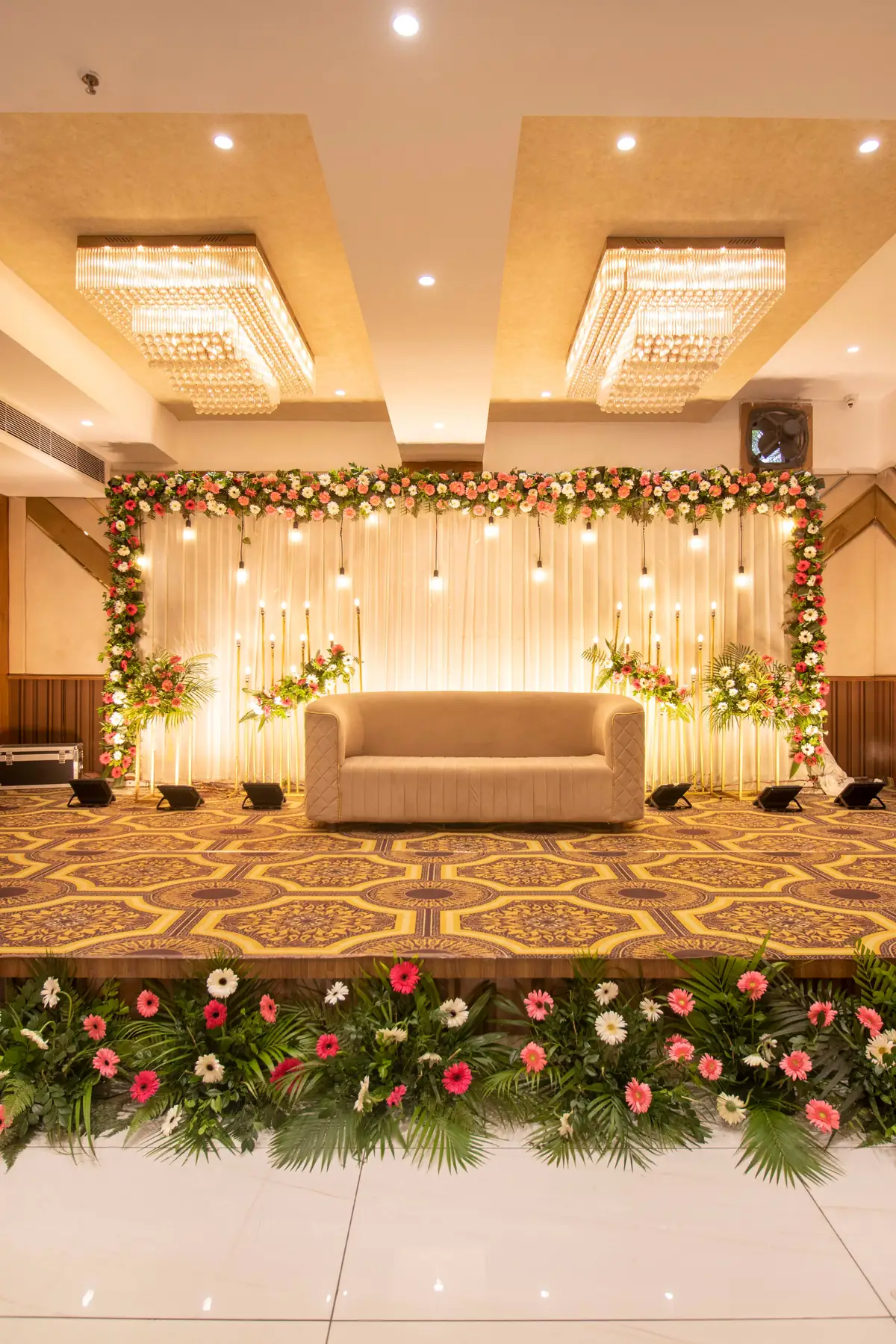 Banquet hall stage with a floral backdrop, hanging lights and a sofa