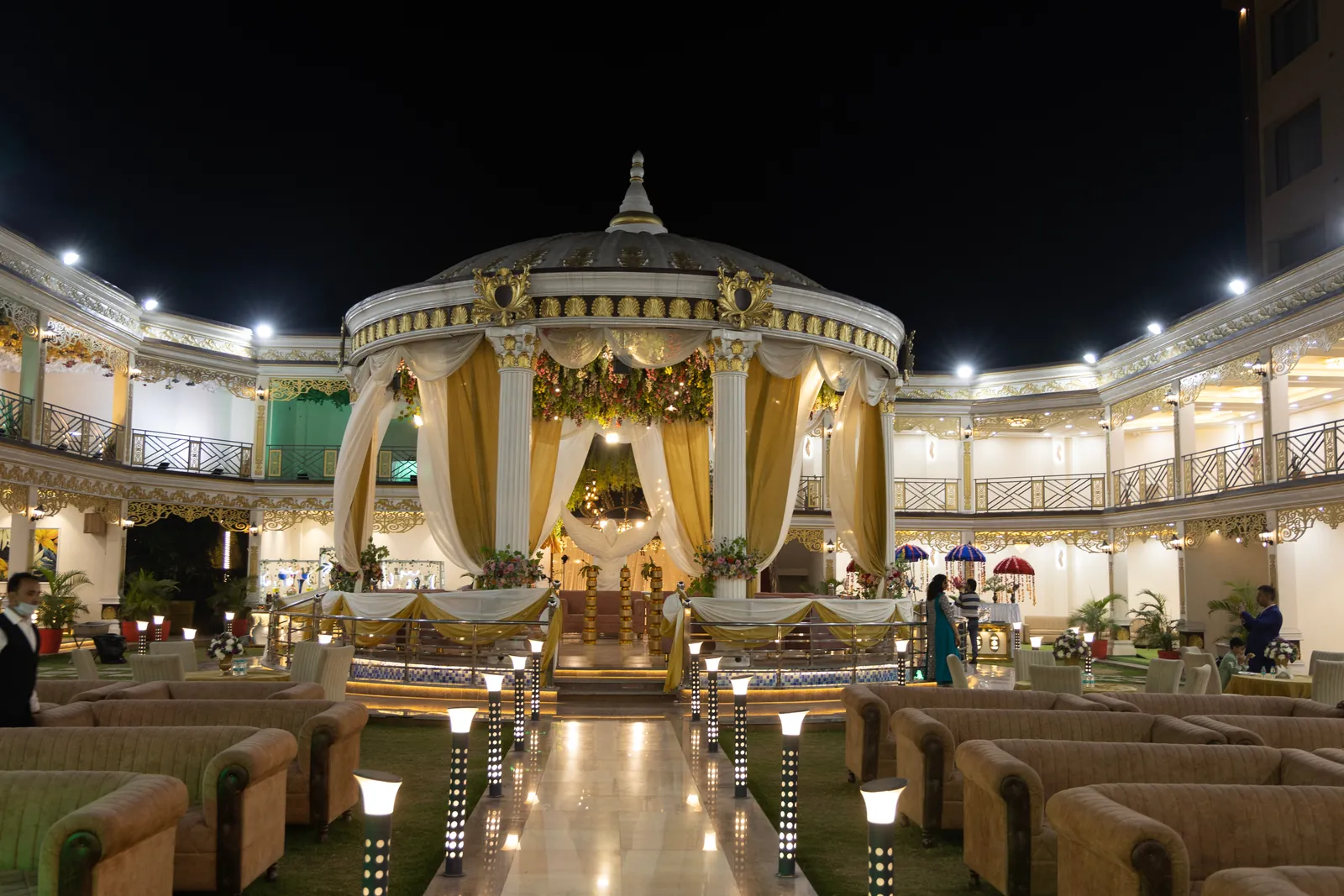 Draped gazebo at the centre of the lawn at night, ringed by a lit two-storey colonnade