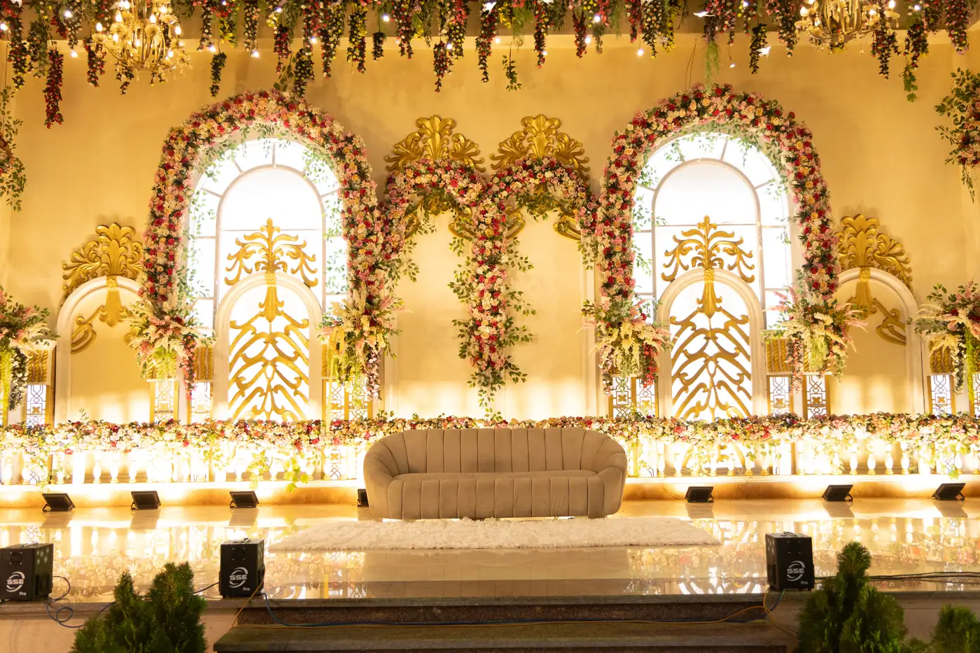 Wedding stage with flower-framed arches and a sofa, lit at night