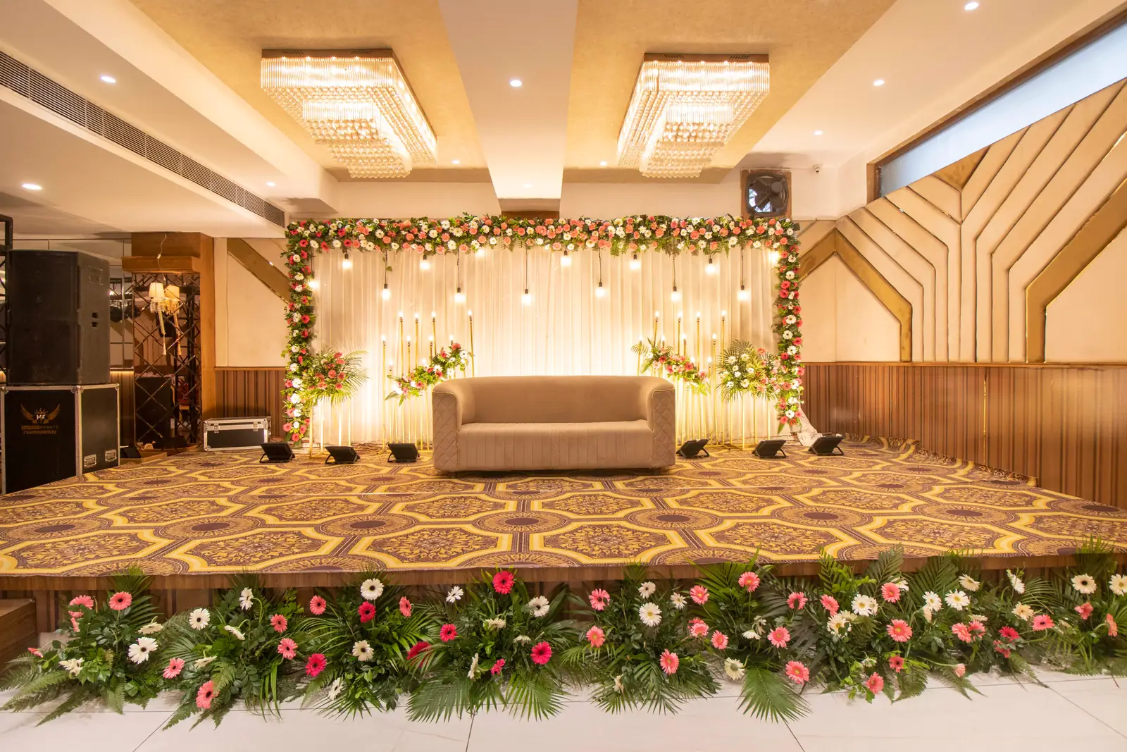 Banquet hall stage with a floral backdrop, hanging lights and a sofa