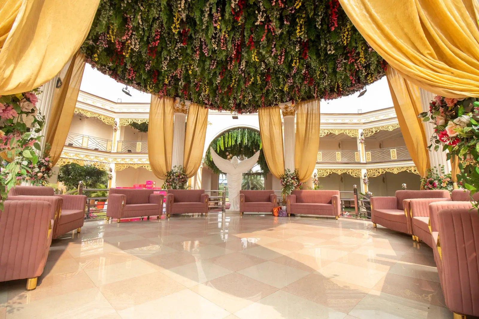 Pavilion with a hanging floral canopy, gold drapes and pink sofa seating