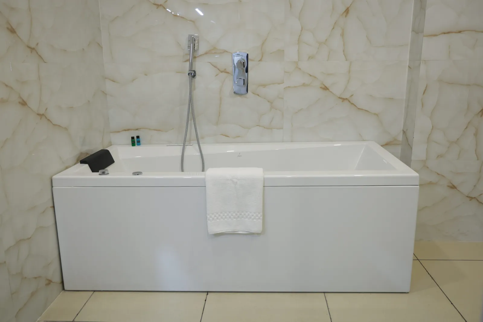 White bathtub with a hand shower against a marble-patterned wall