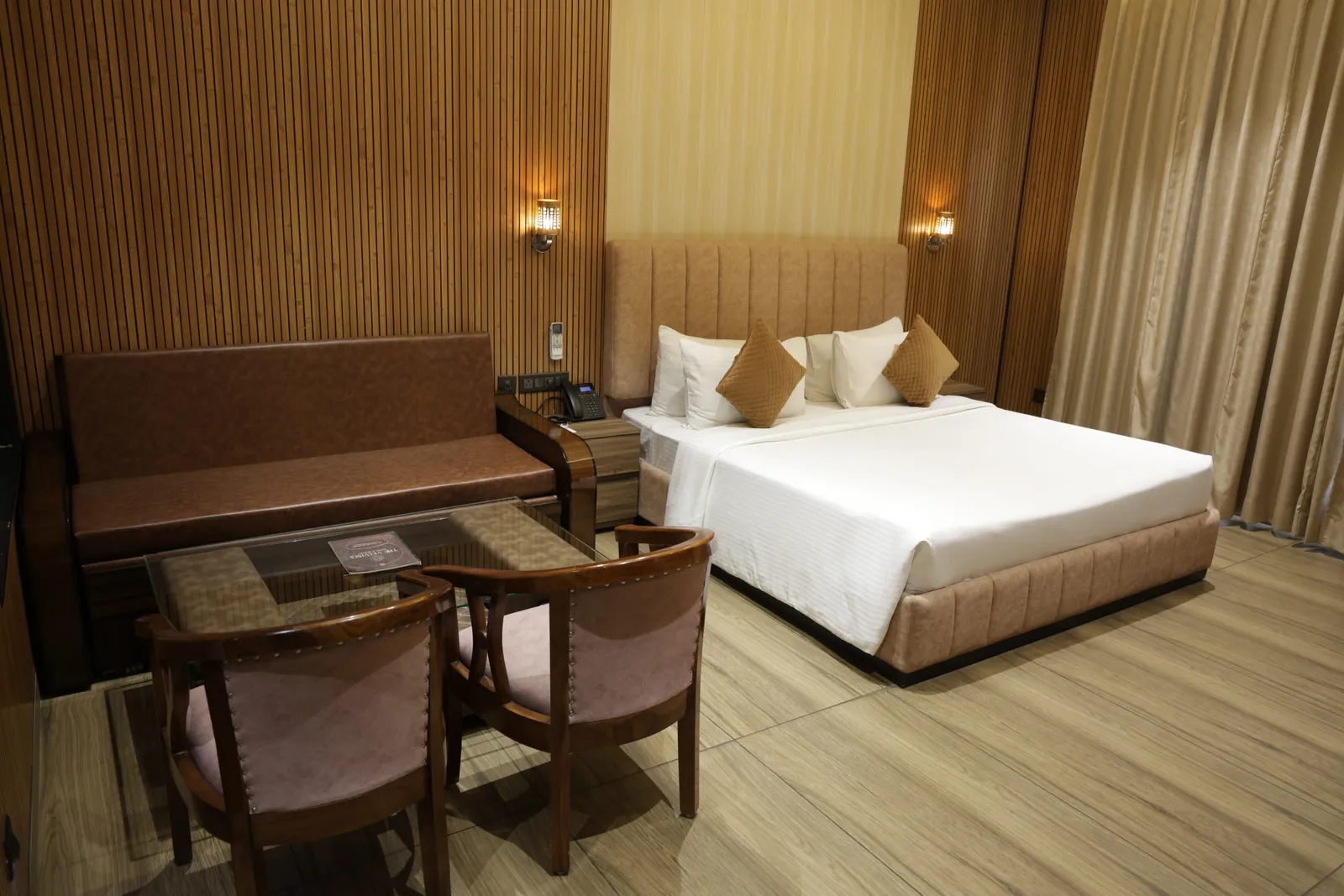 Wood-panelled guest room with a double bed, sofa and a glass table with two chairs